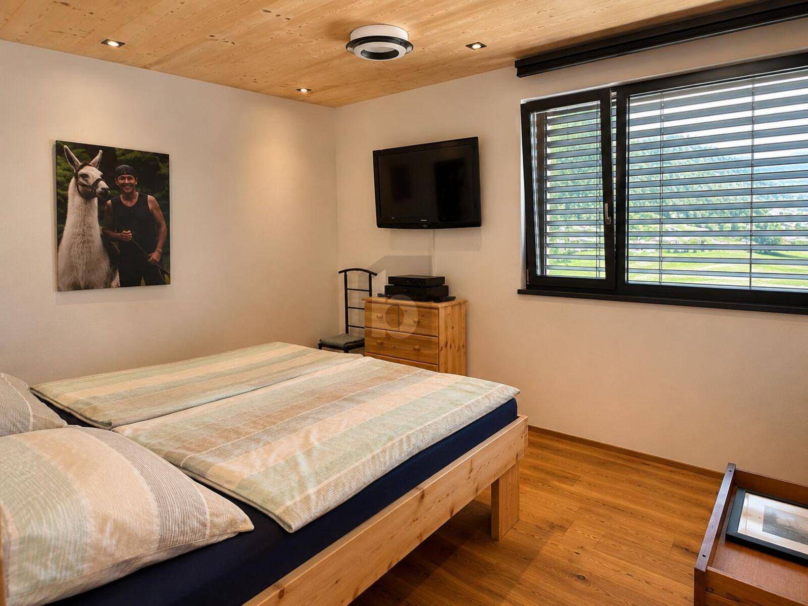 Gemütliches Schlafzimmer mit Holzboden, Holzdecke und einem Fenster mit Blick ins Grüne.