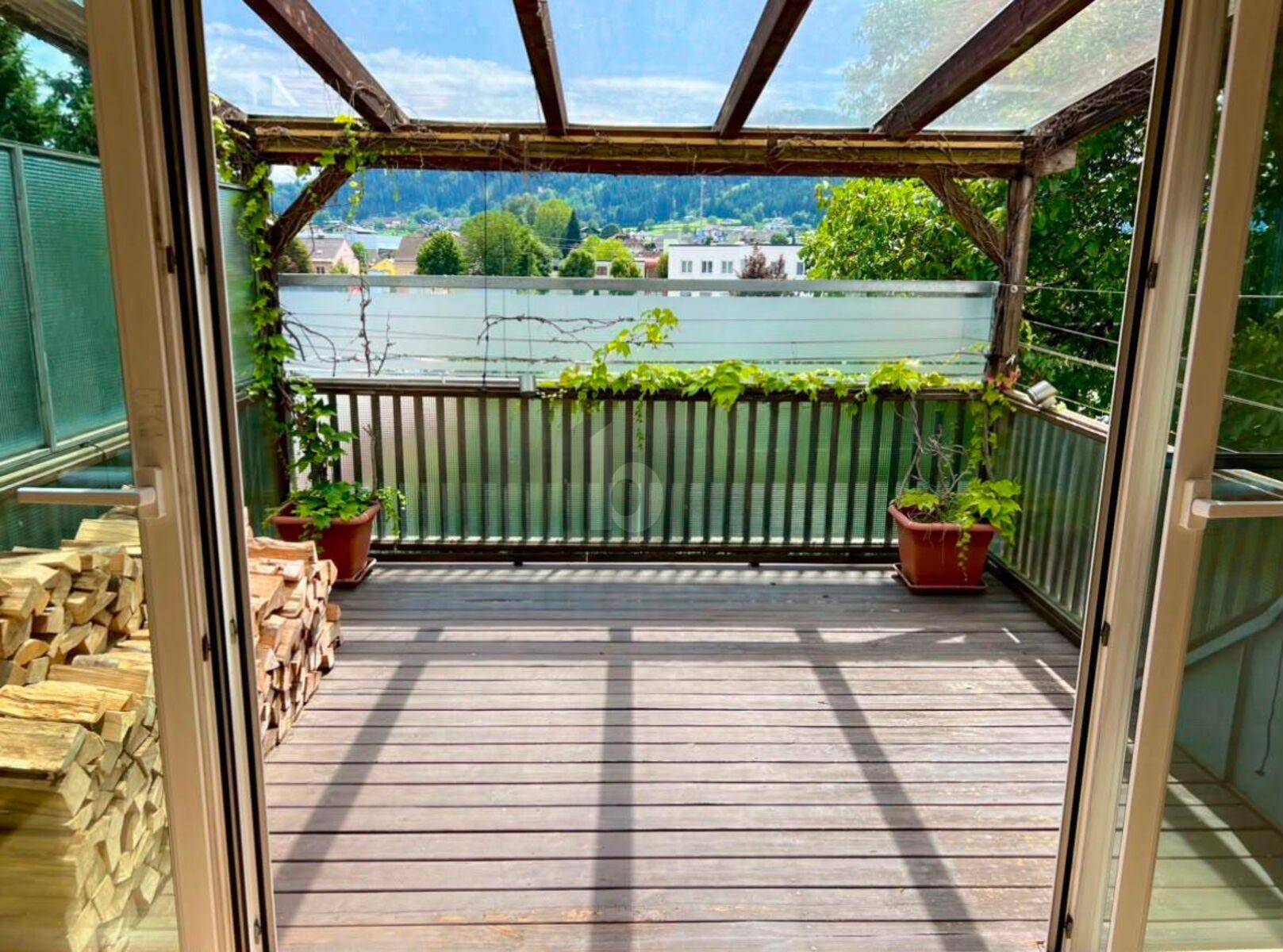Überdachte Holzterrasse mit Blick ins Grüne und gestapeltem Brennholz.