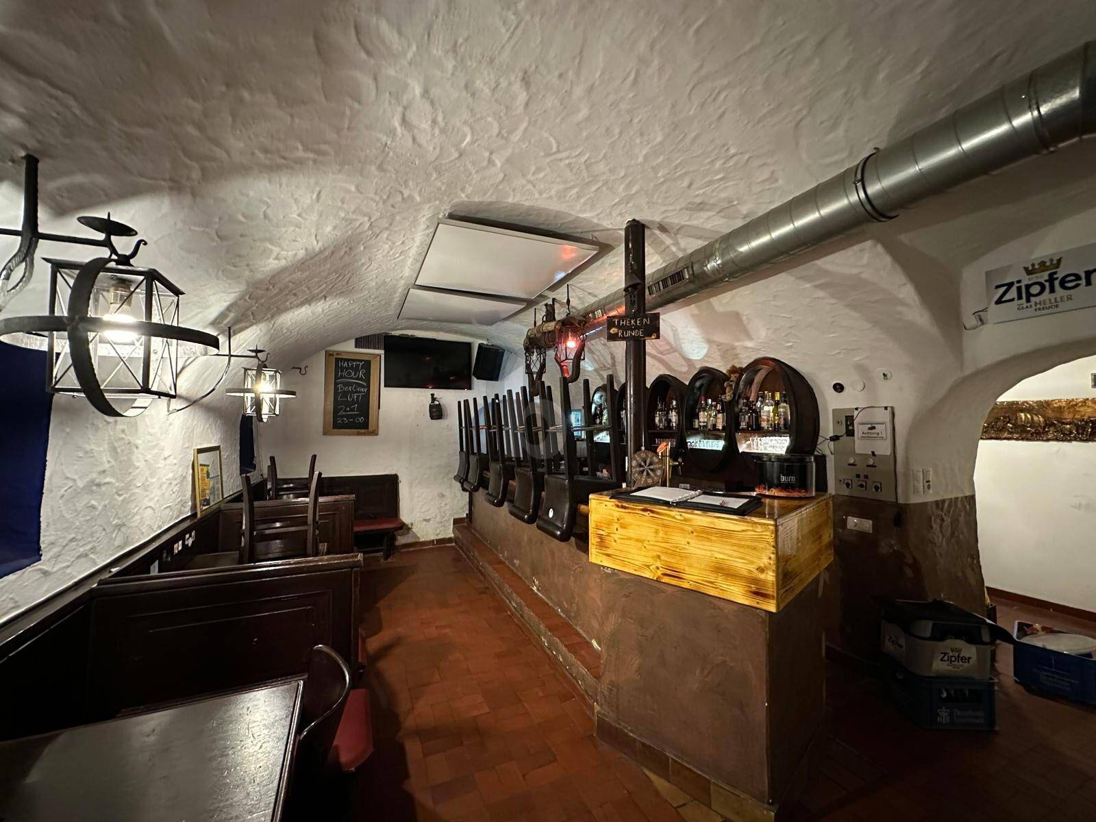 Traditioneller Barbereich mit Holztresen, Hockern und einer gewölbten Decke mit sichtbaren Lüftungsrohren.