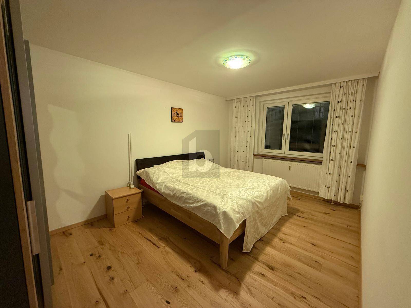 Schlafzimmer mit Doppelbett, Nachttisch und einem Fenster, ausgestattet mit Vorhängen und Holzboden.