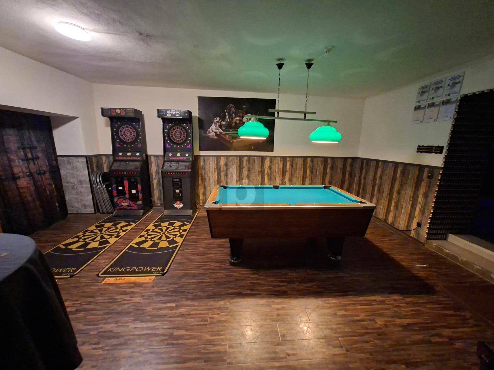 Geräumiger Spielraum mit Billardtisch, Dartautomaten und Holzvertäfelung an den Wänden.