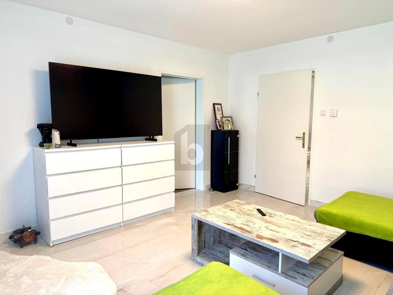 Modernes Wohnzimmer mit großem Fernseher auf weißer Kommode und Fliesenboden.