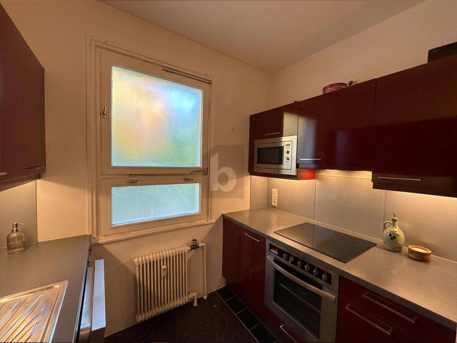 Kleine Küche mit dunkelroten Schränken, integrierten Geräten und einem Fenster, das Tageslicht spendet.