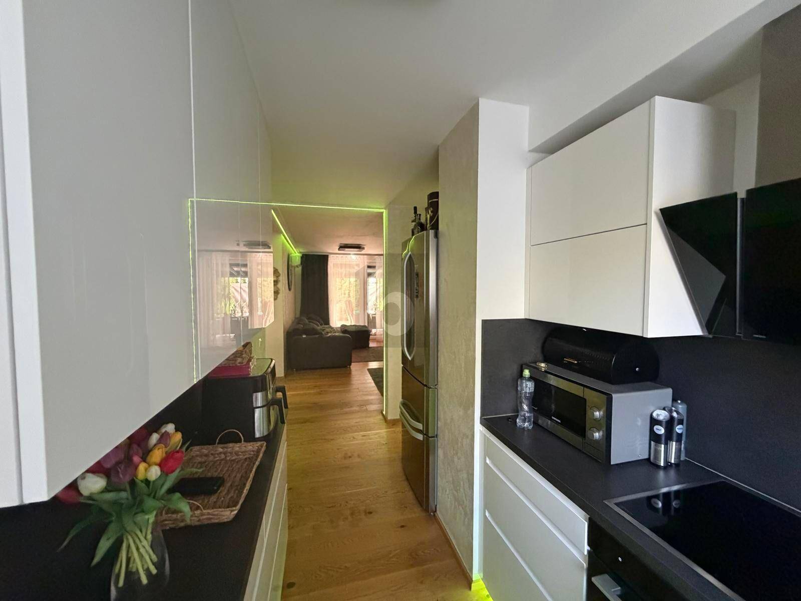 Moderne Küchenzeile mit weißen Schränken, Edelstahlkühlschrank und Holzboden, führt zum Wohnbereich.