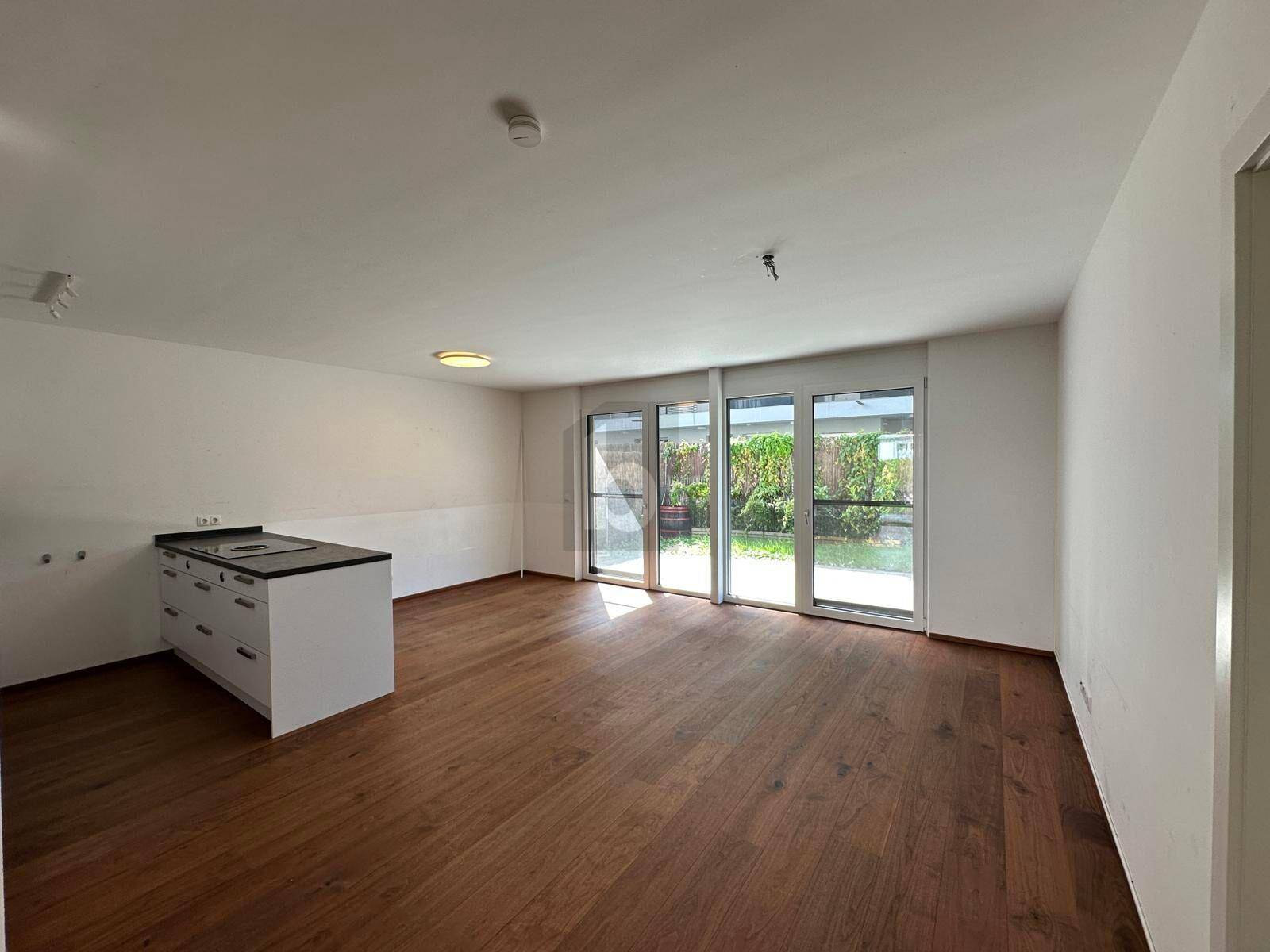 Heller offener Wohnbereich mit Holzboden, teilweiser Kücheninsel und Zugang zum Garten.