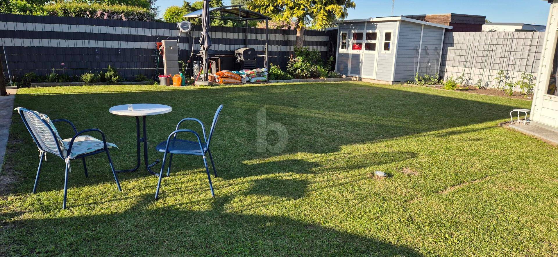 Gepflegter Garten mit Rasenfläche, Gartenmöbeln und einem Gartenhaus im Hintergrund, ideal zum Entspannen.