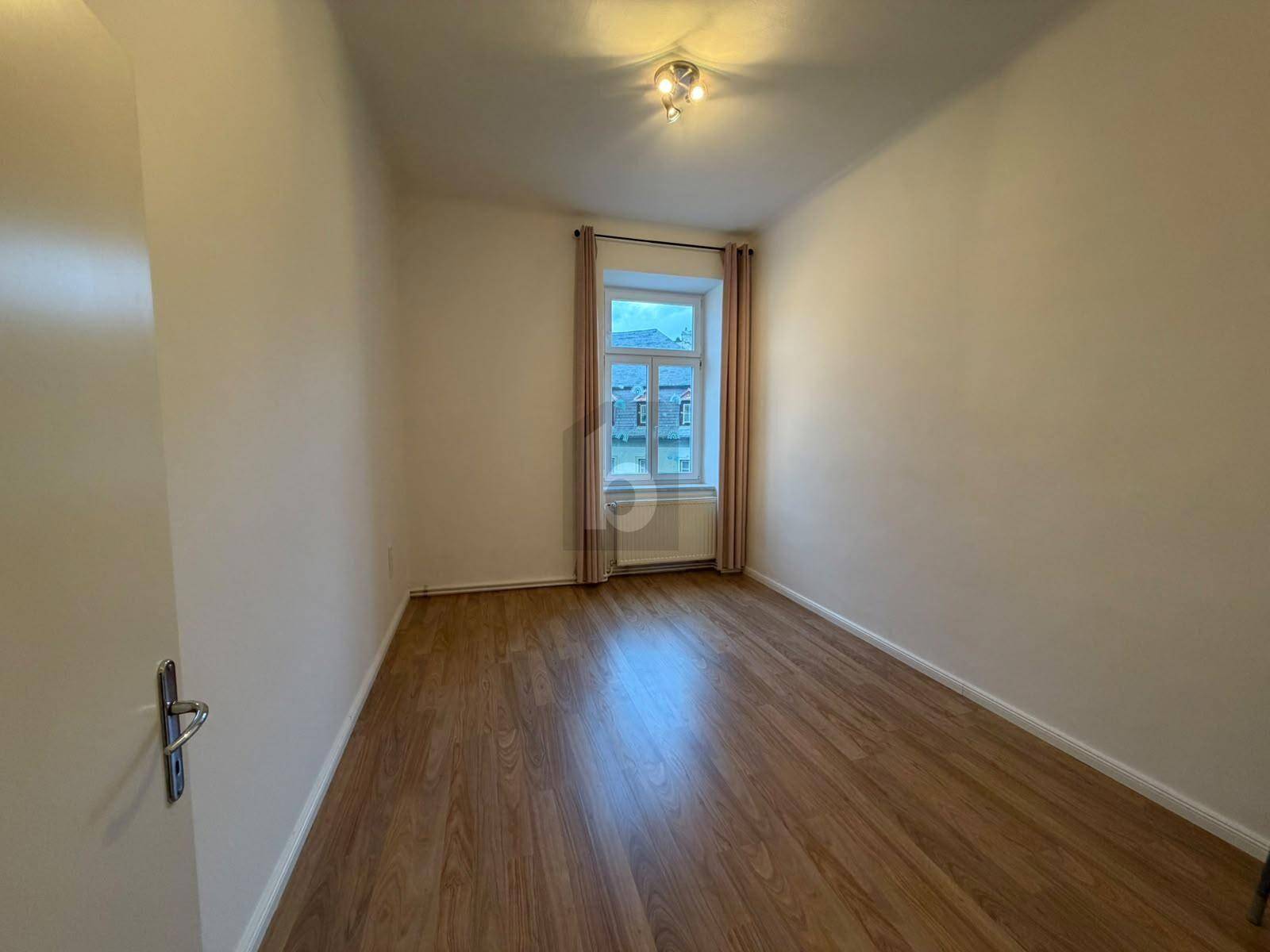 Leeres Zimmer mit Holzboden und einem Fenster, bereit zur individuellen Einrichtung und Nutzung.