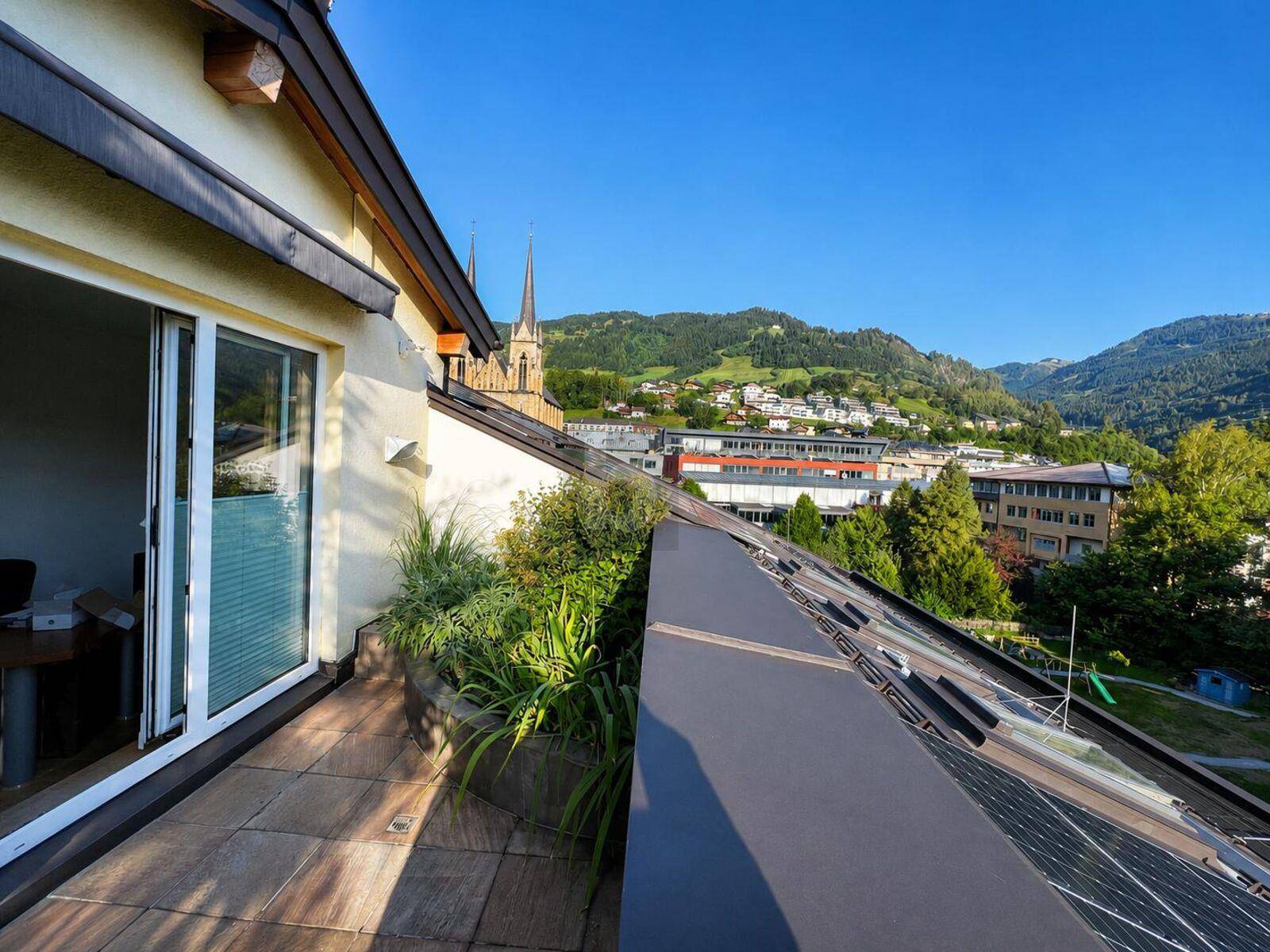 Langer Balkon mit Fliesenboden und Bepflanzung, der einen Blick auf die Stadt und die Berge im Hintergrund bietet.