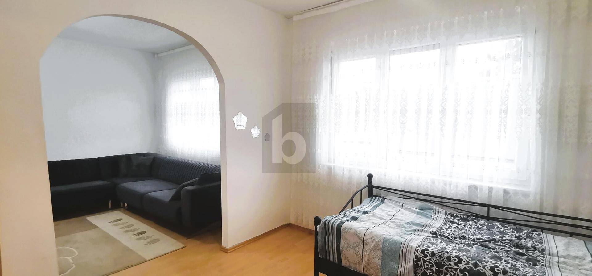 Schlafzimmer mit Bett und einem offenen Durchgang zu einem weiteren Wohnbereich mit Sofa.
