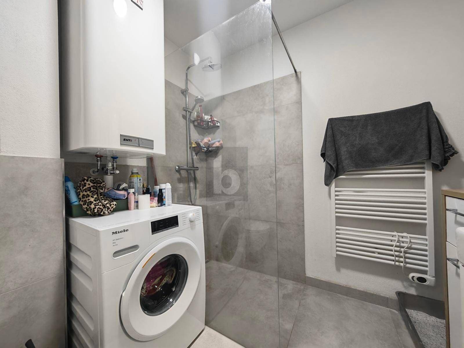 Modernes Badezimmer mit ebenerdiger Dusche, Waschmaschine und beheiztem Handtuchhalter.