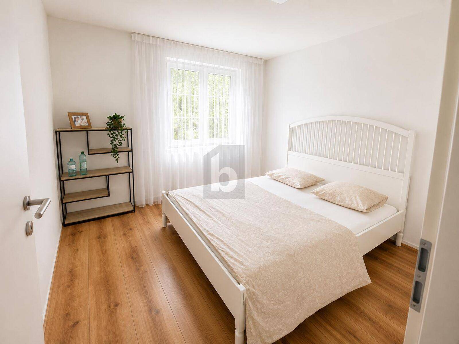 Helles Schlafzimmer mit Holzboden, weißem Bett und Blick ins Grüne durch das Fenster.