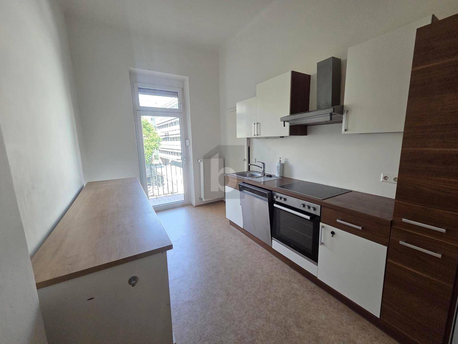 Funktionale Einbauküche mit weißen und holzfarbenen Schränken sowie Zugang zu einem Balkon.