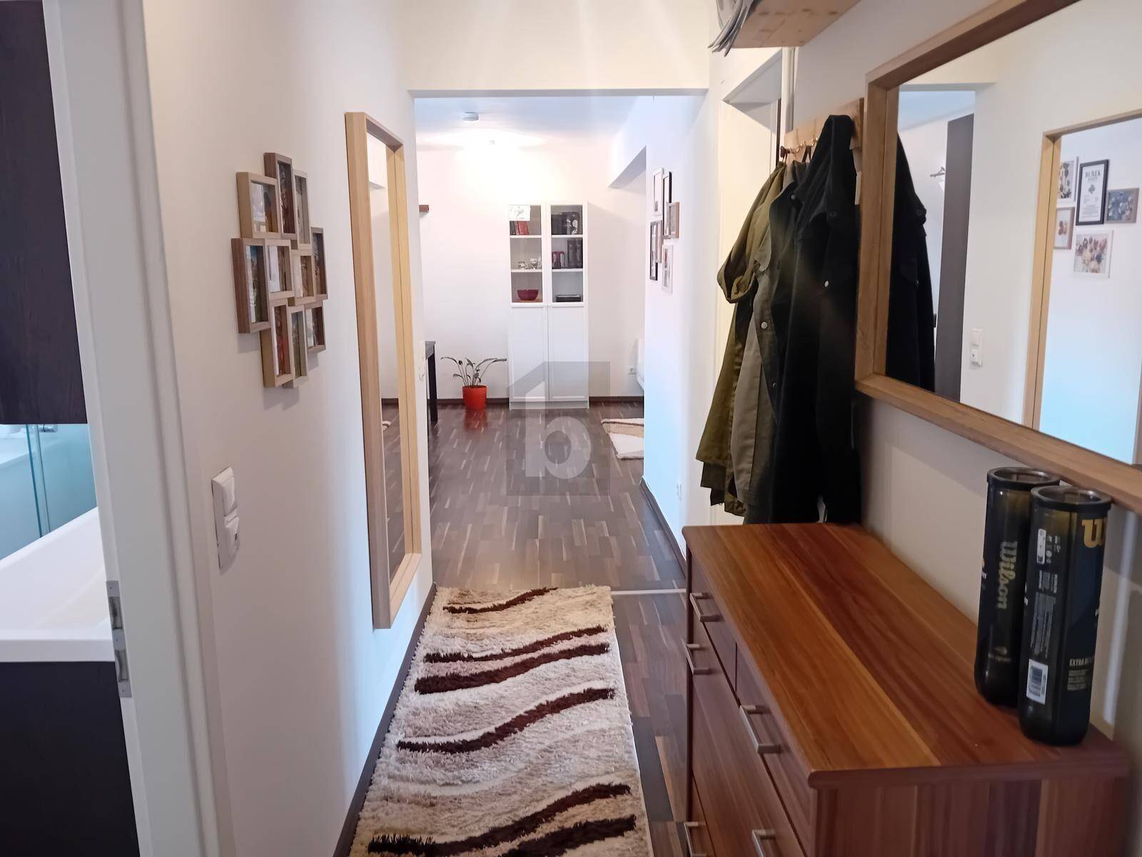 Heller Flur mit Holzkommode, Spiegel und Garderobe, der in den Wohnbereich führt.
