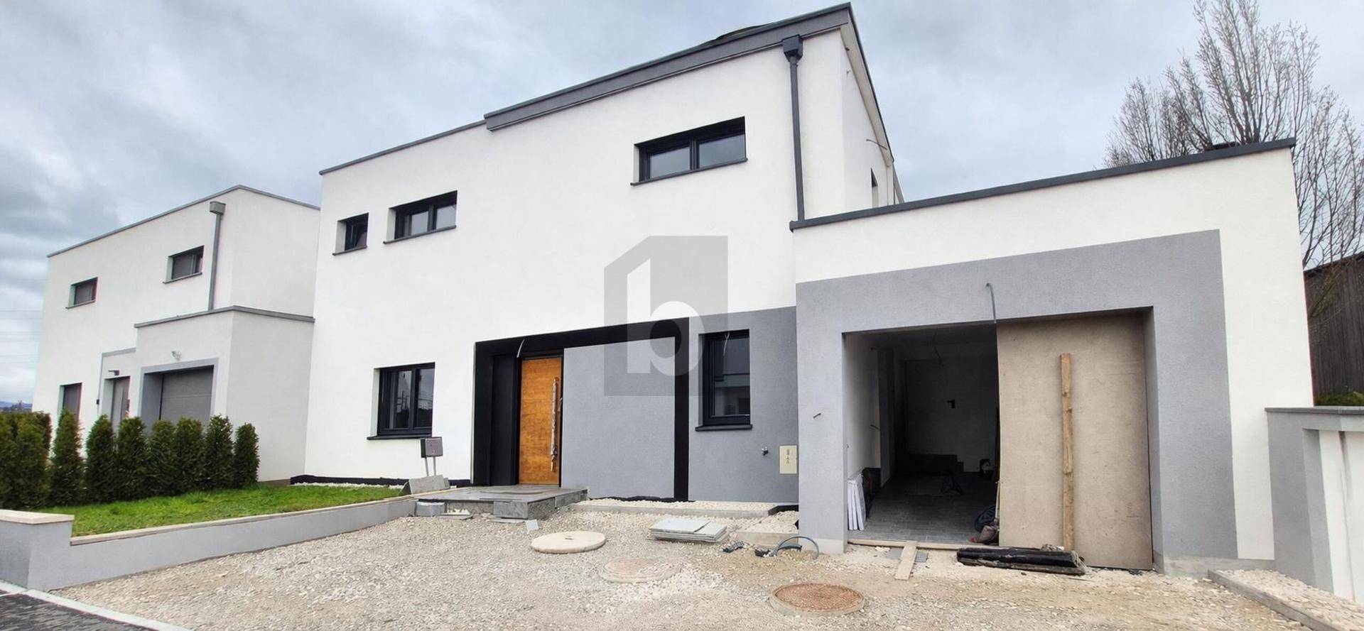 Moderne weiße Doppelhaushälfte im Bau mit Garage und schlichter Architektur.