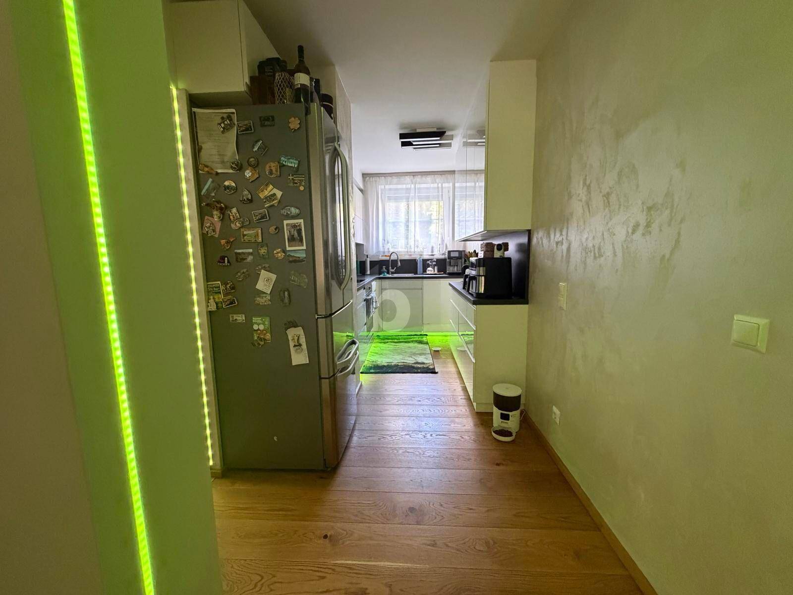 Helle Küchenzeile mit Edelstahlkühlschrank, weißen Schränken und Fensterblick, gut beleuchtet.