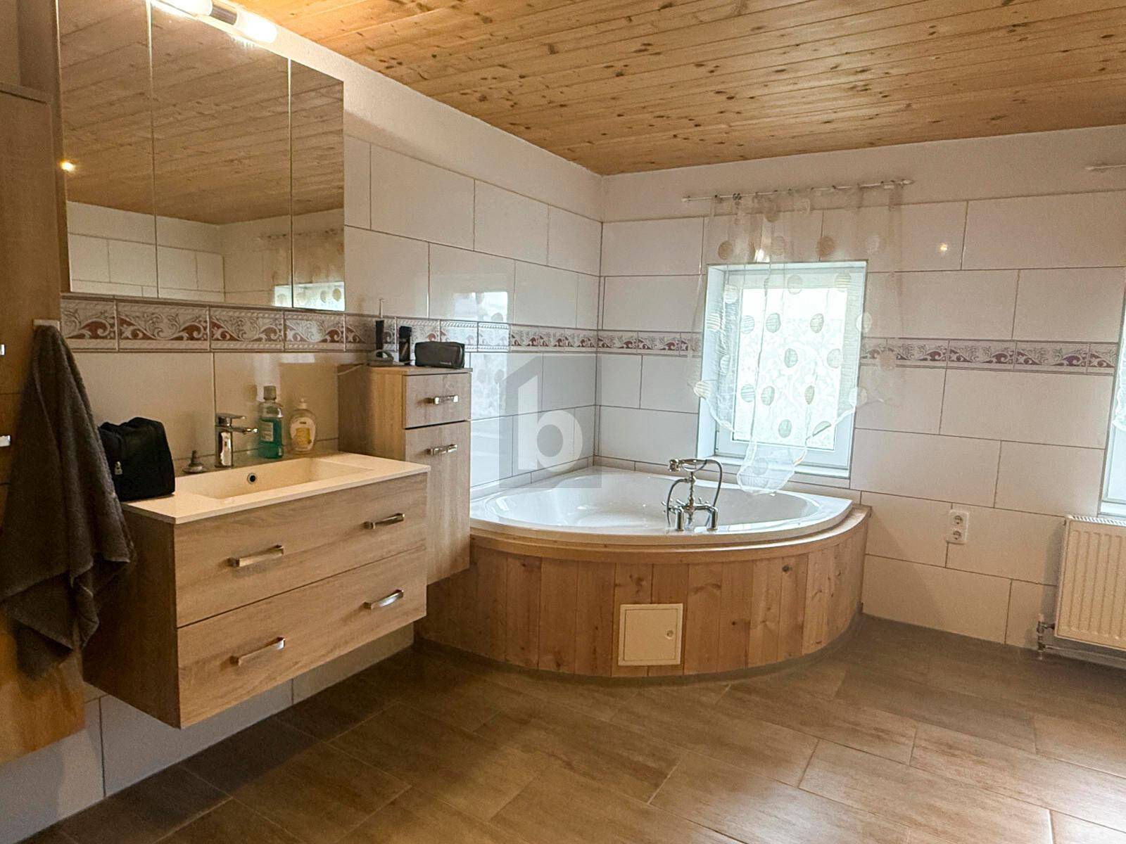 Helles Badezimmer mit Eckbadewanne, Holzverkleidung, schwebendem Waschtisch und Fenster.
