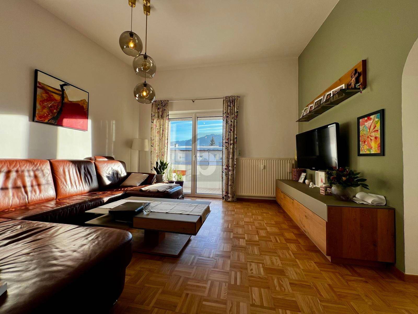 Gemütliches Wohnzimmer mit Ledersofa, Parkettboden und direktem Zugang zu einem sonnigen Balkon.