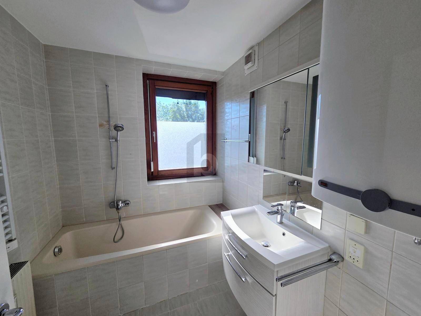 Gefliestes Badezimmer mit Badewanne, Einzelwaschbecken und Fenster für Tageslicht.