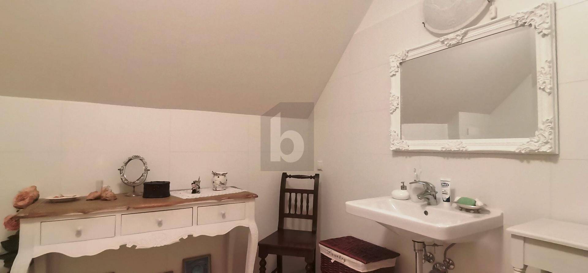 Helles Badezimmer mit Waschbecken, großem Spiegel und einem Schminktisch unter der Dachschräge.