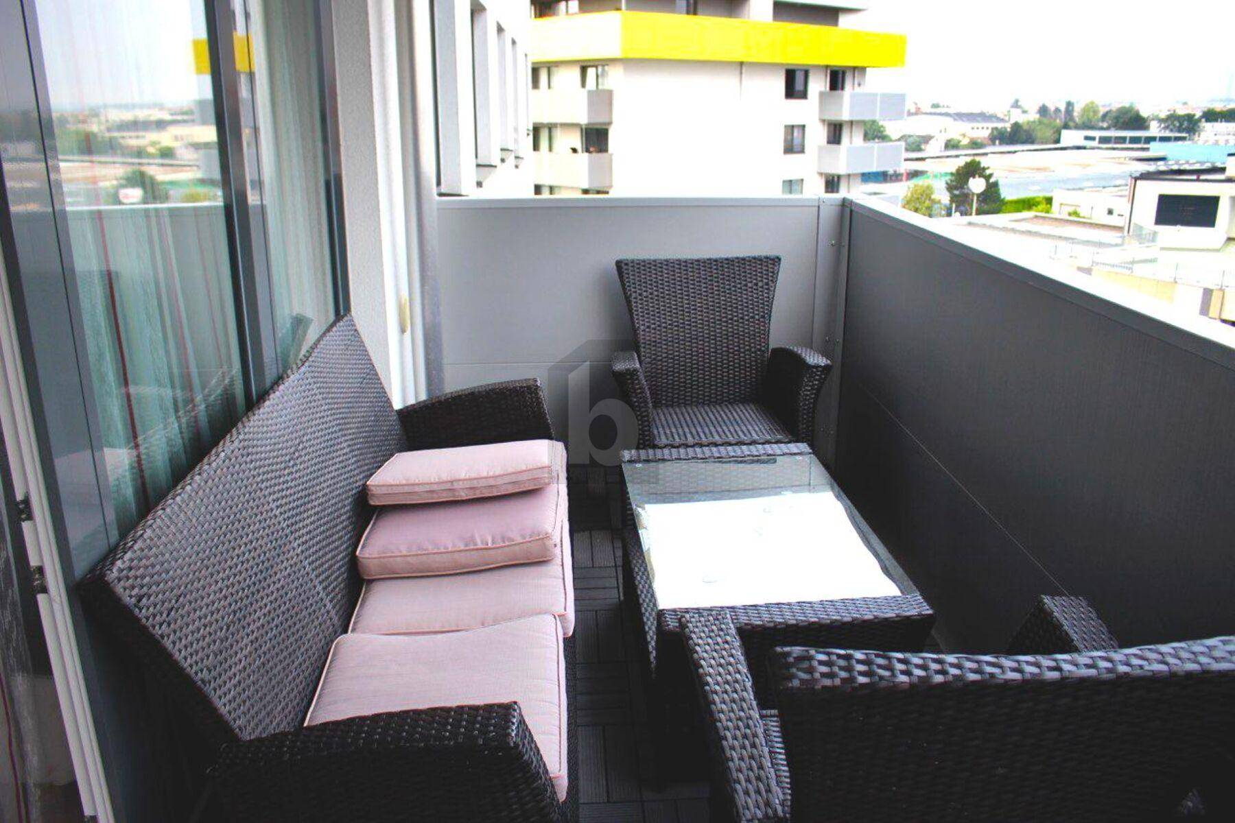 Möblierter Balkon mit Rattanmöbeln und Blick auf die umliegenden Gebäude.