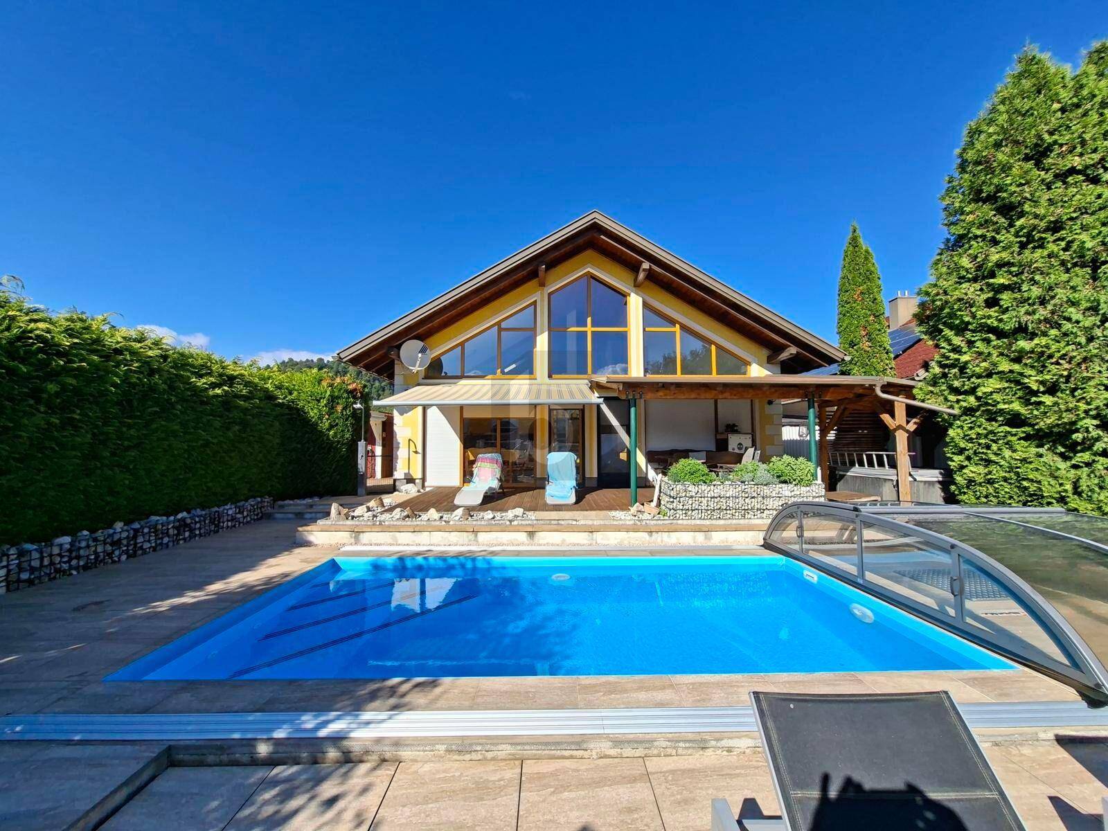 Außenansicht des Hauses mit großem Pool, Liegestühlen und gepflegtem Gartenbereich unter blauem Himmel.