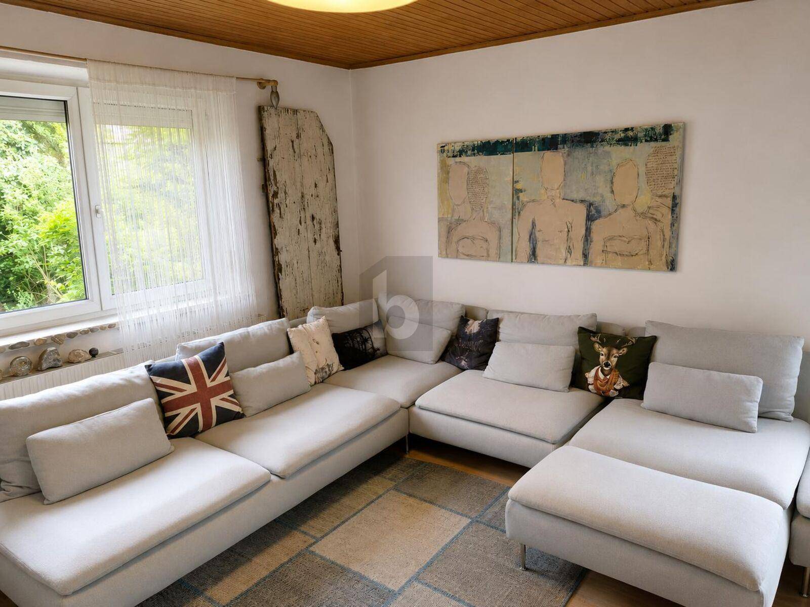 Helles Wohnzimmer mit großem Ecksofa, Holzbalkendecke und Blick ins Grüne.