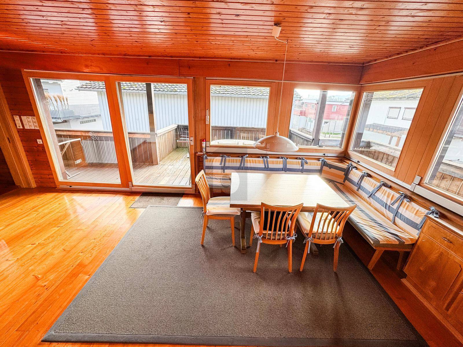 Heller Essbereich mit Holzboden, großer Eckbank und Zugang zu einem Außenbalkon.