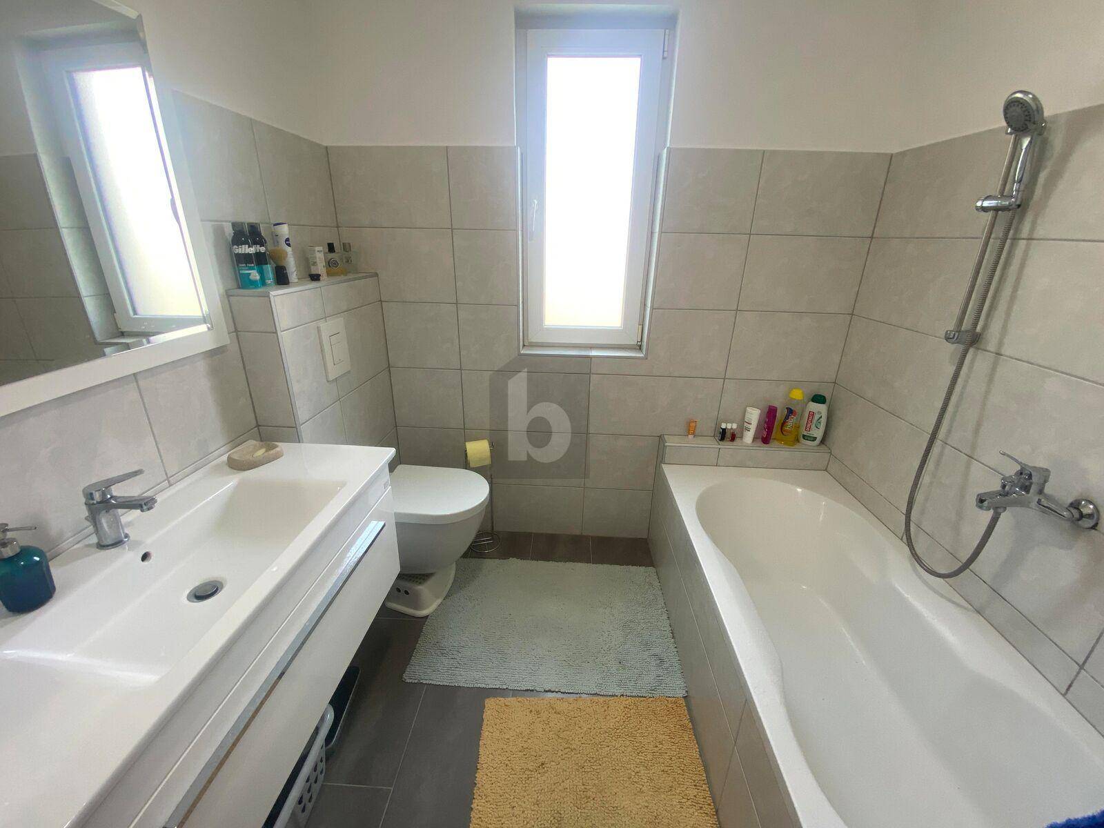 Modernes Badezimmer mit Badewanne, Waschbecken, Toilette und einem hohen Fenster für Tageslicht.