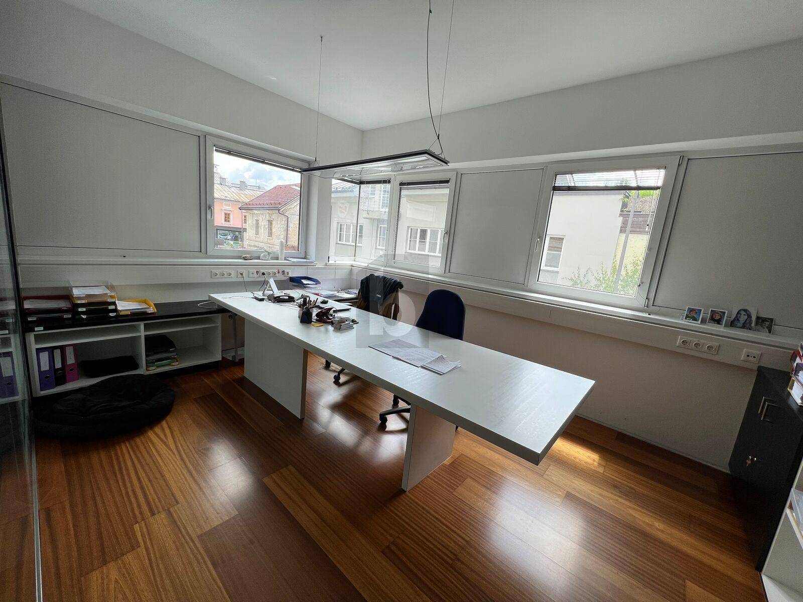 Einzelner Arbeitsplatz in einem hellen Büro mit breitem Schreibtisch, Holzfußboden und Fensterblick.