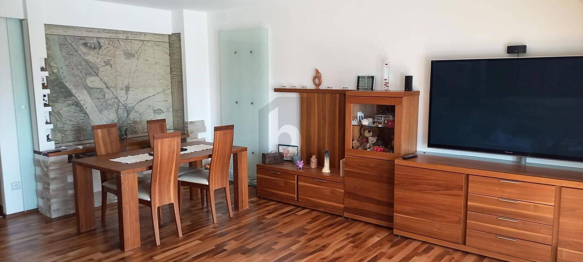 Geräumiger Wohn-Essbereich mit Holztisch, passenden Möbeln und einem großen Fernseher an der Wand.