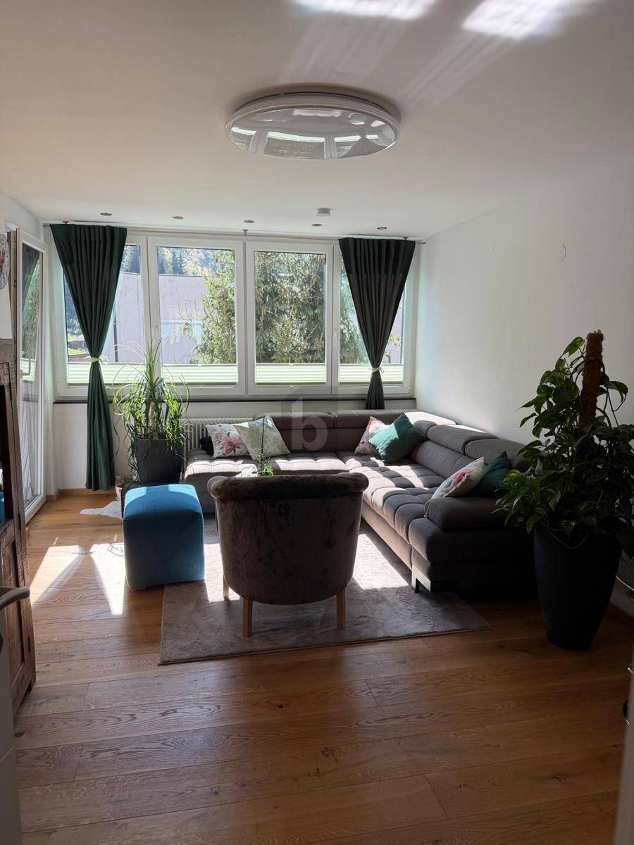 Lichtdurchflutetes Wohnzimmer mit bequemer Sitzecke, Holzboden und grünen Vorhängen.