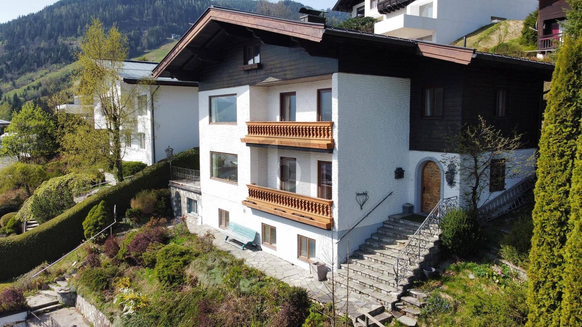Traditionelles Haus mit weißer Fassade, Holzbalkonen und Satteldach in Hanglage.