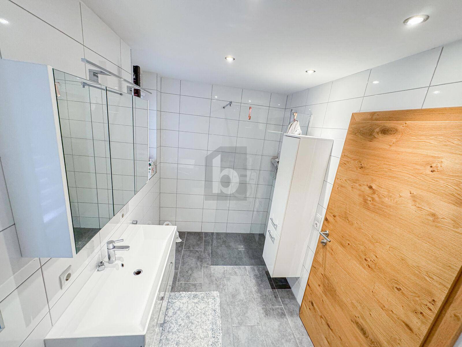Modernes Badezimmer mit weißen Wandfliesen, großem Waschbecken und begehbarer Dusche.