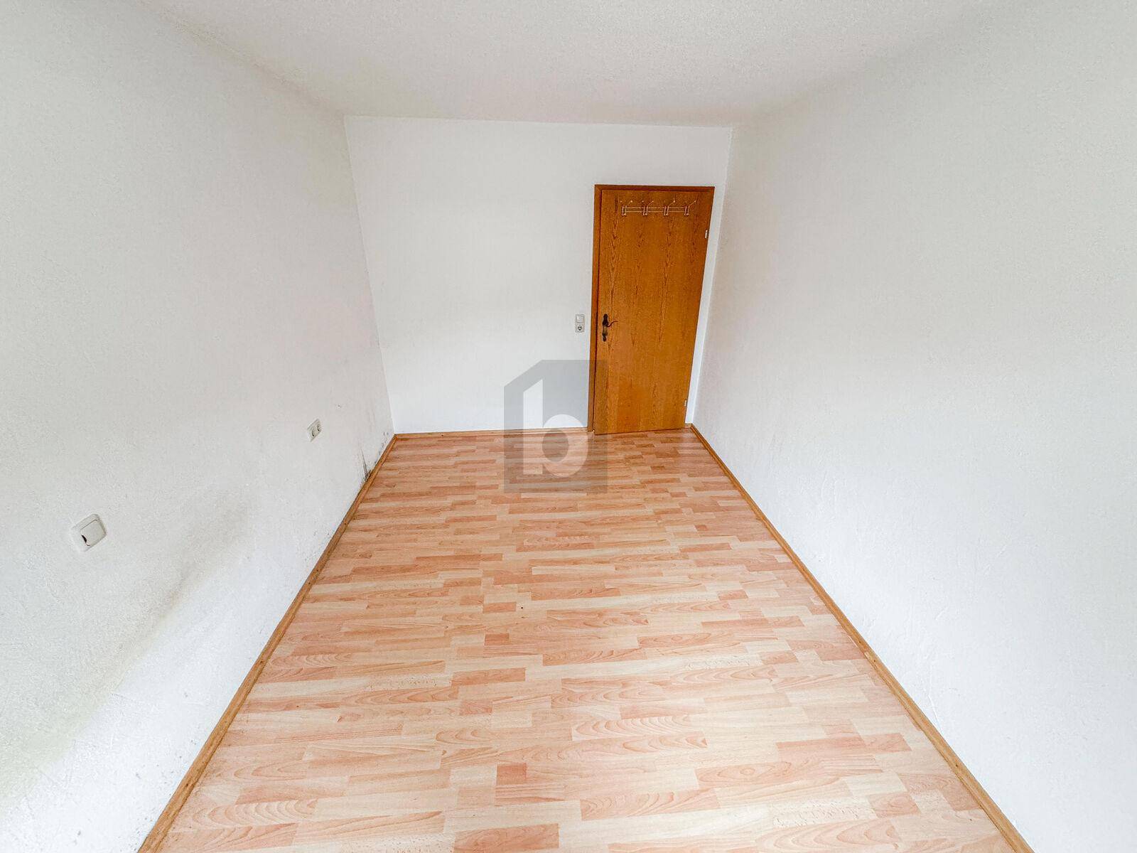 Leerer Raum mit Laminatboden und einer Holztür, bereit zur individuellen Gestaltung.