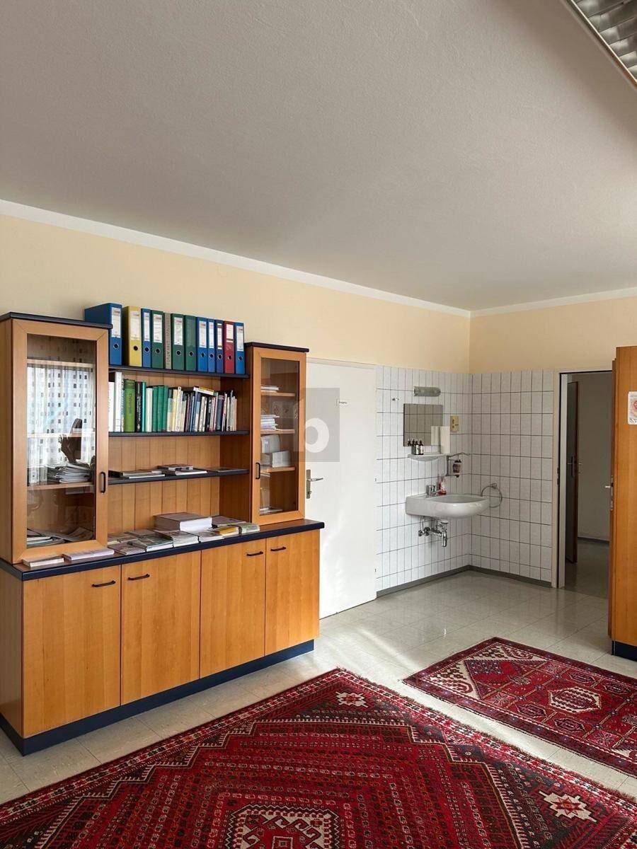 Raum mit großem Holzschrank, zwei Teppichen und einem Waschbeckenbereich mit weißen Fliesen.