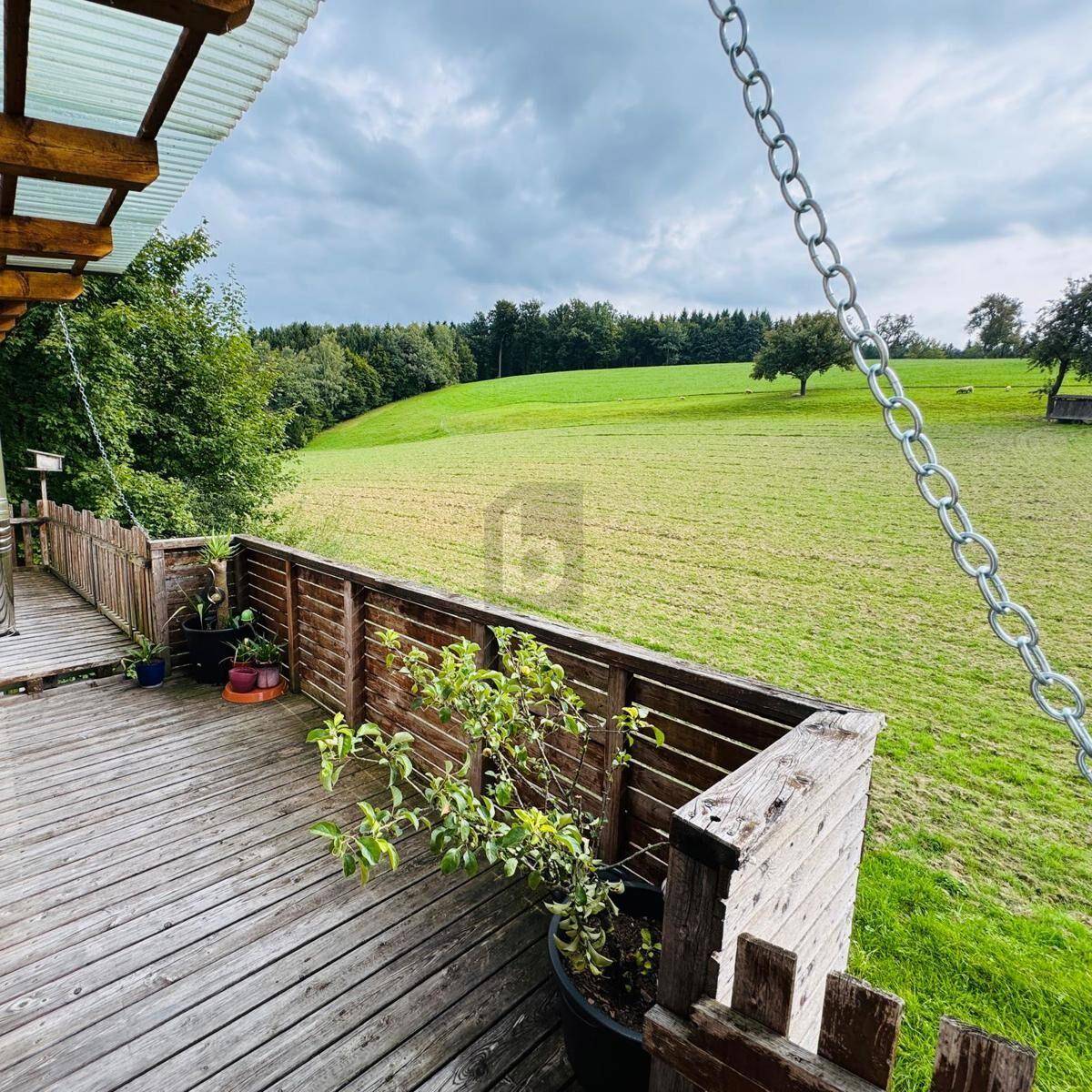 Holzterrasse mit Blick auf grüne Wiesen und bewaldete Hügel.