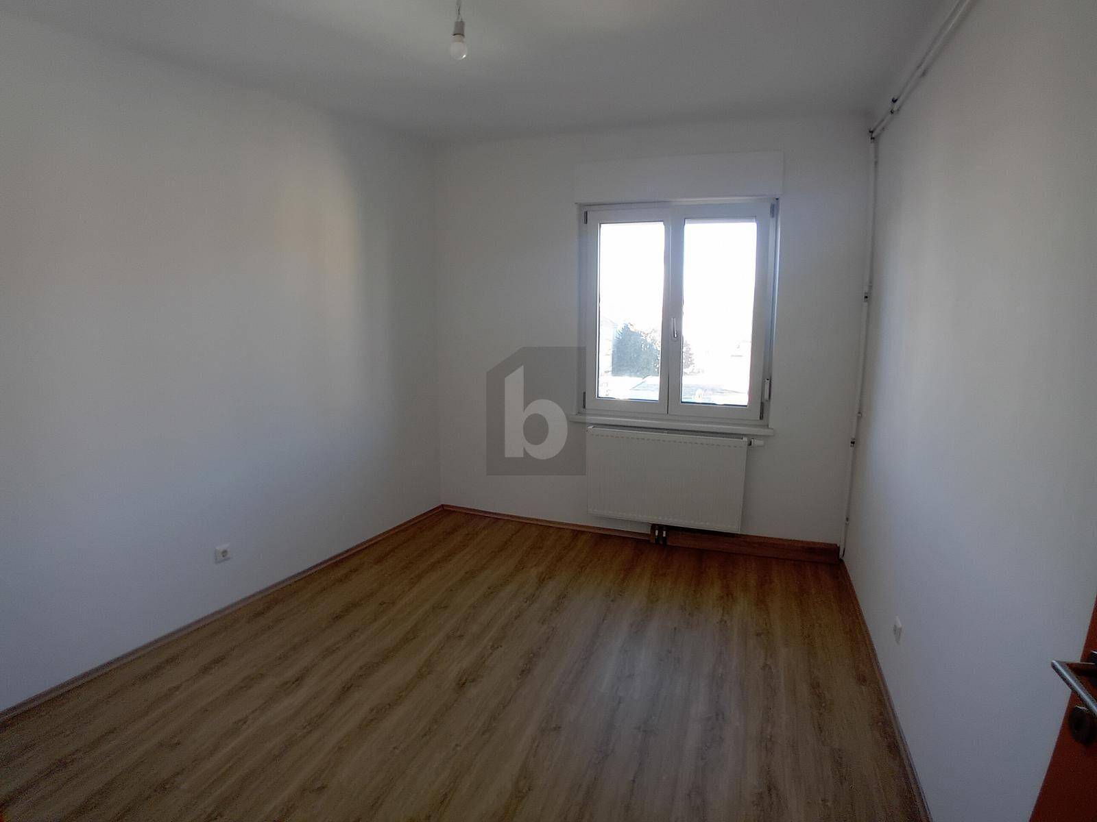 Leeres Zimmer mit Laminatboden und einem Fenster, das für gute Belichtung sorgt.