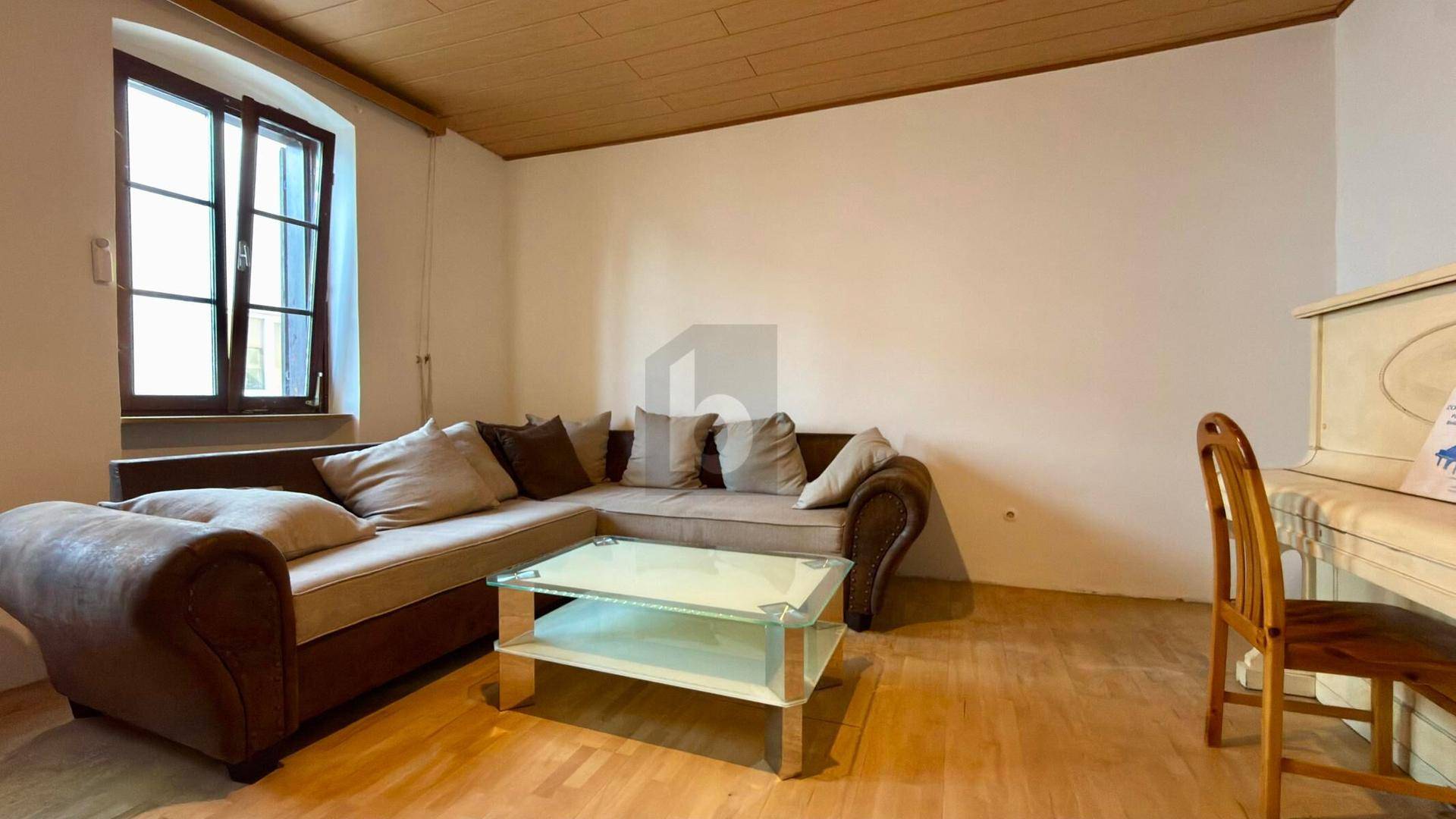 Gemütliches Wohnzimmer mit großem Ecksofa, Couchtisch, Holzboden und einem Fenster für natürliches Licht.