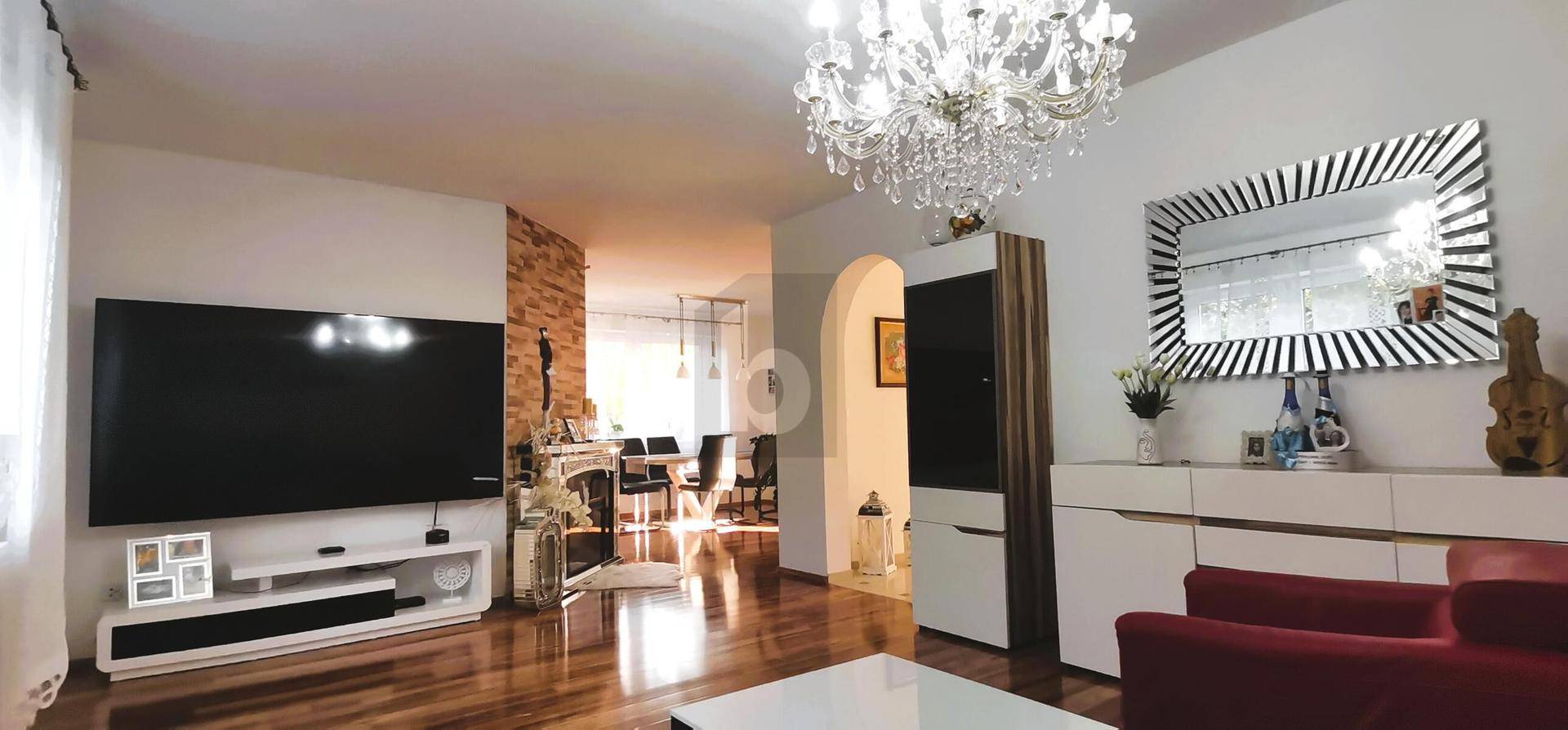 Elegantes Wohnzimmer mit Kronleuchter, großem Fernseher und Holzboden in warmen Farbtönen.