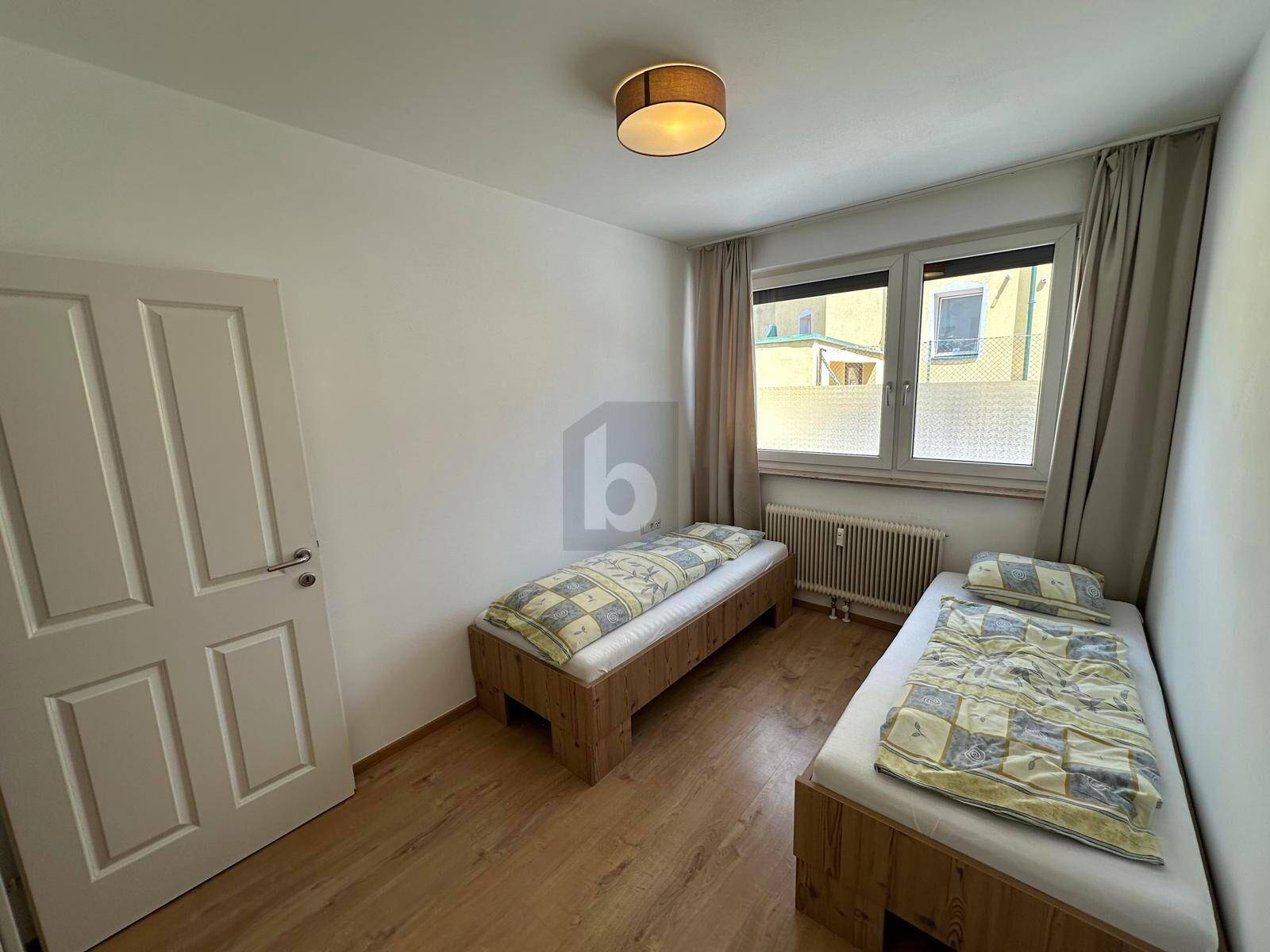 Helles Schlafzimmer mit zwei Einzelbetten, Holzboden und Fenster mit Blick nach draußen.