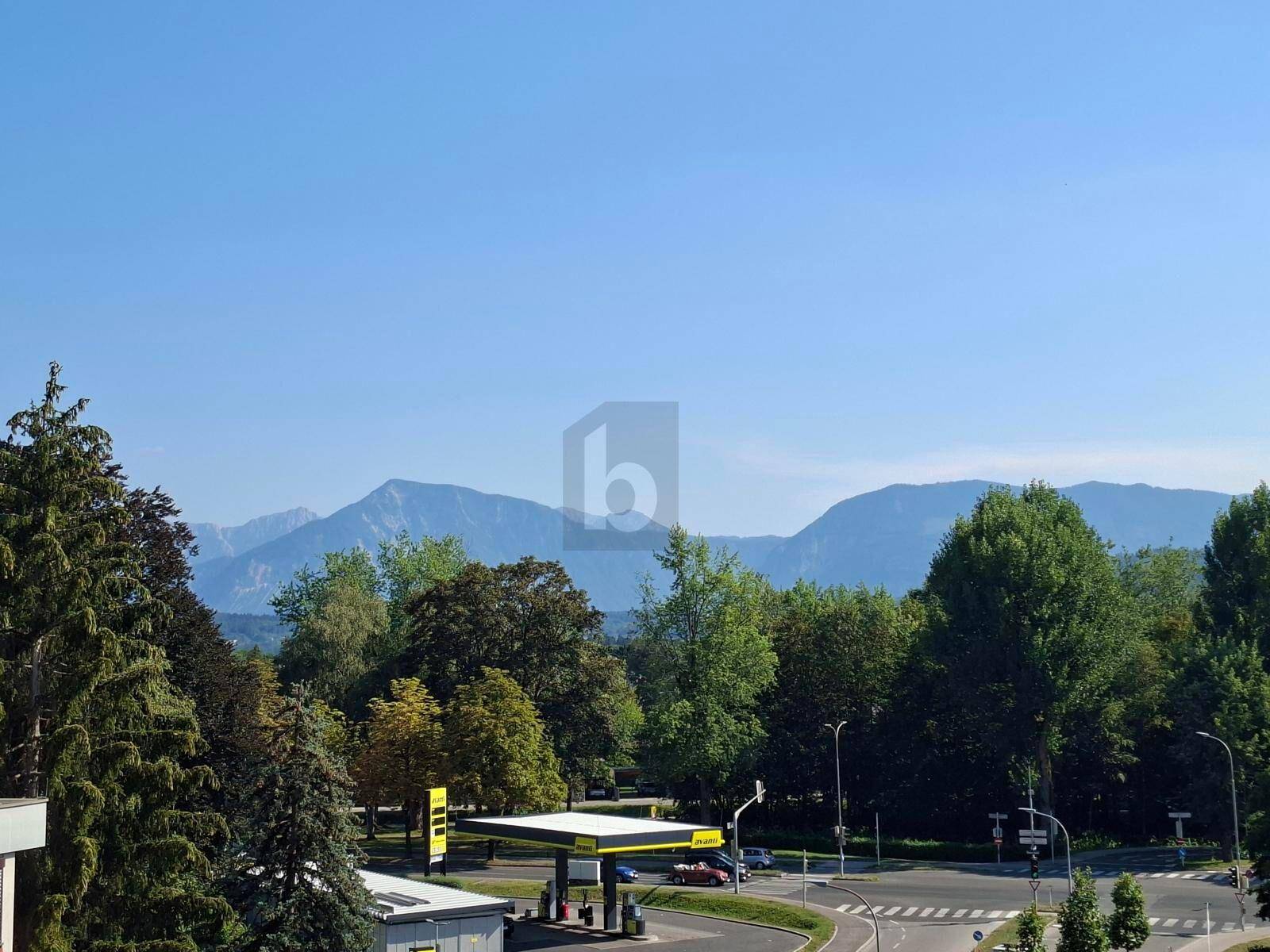 Weitläufiger Blick auf die umliegende Berglandschaft und grüne Bäume unter blauem Himmel.