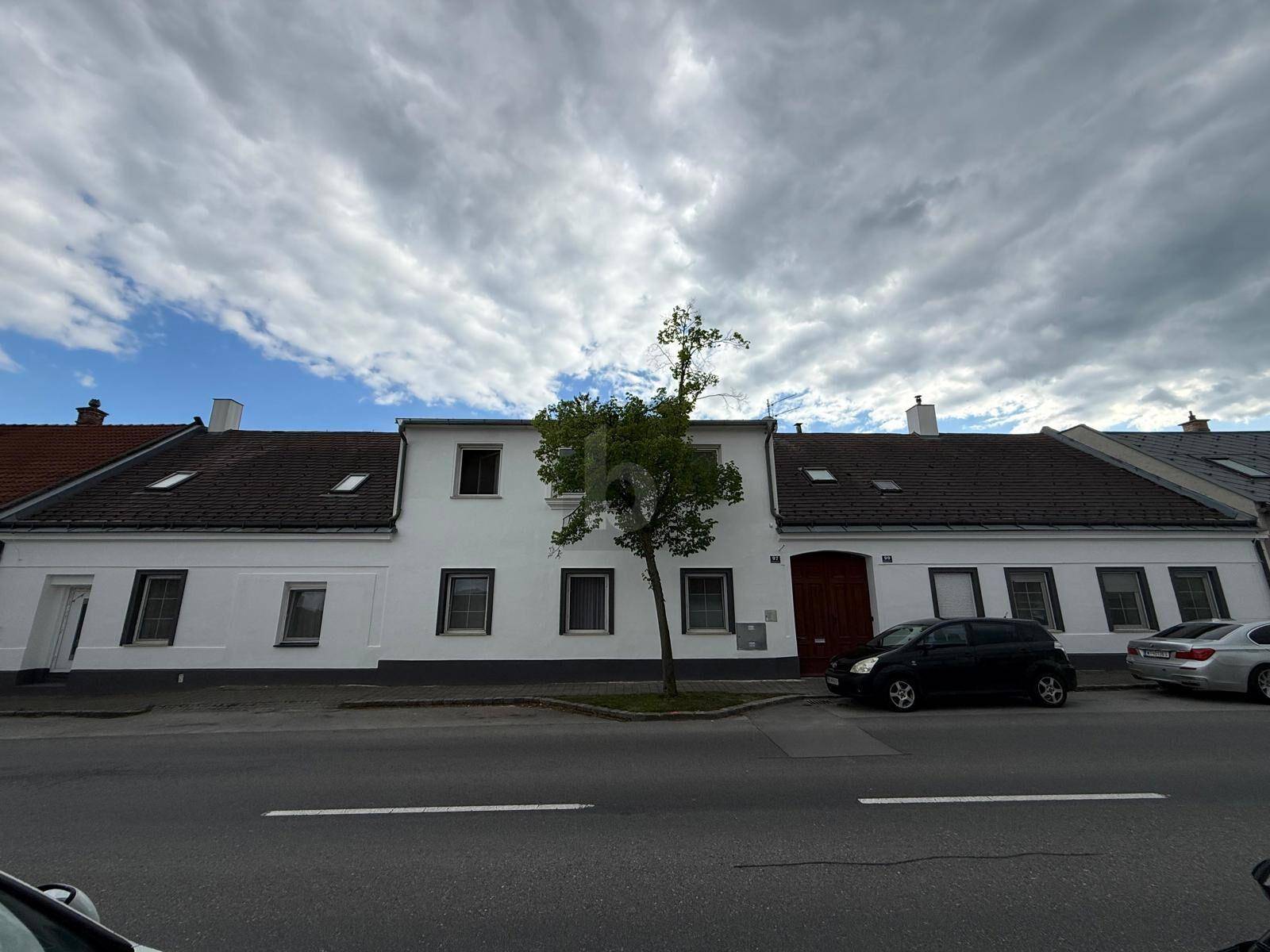 Weiße Fassade eines traditionellen Gebäudes mit Satteldach und geparkten Autos davor.