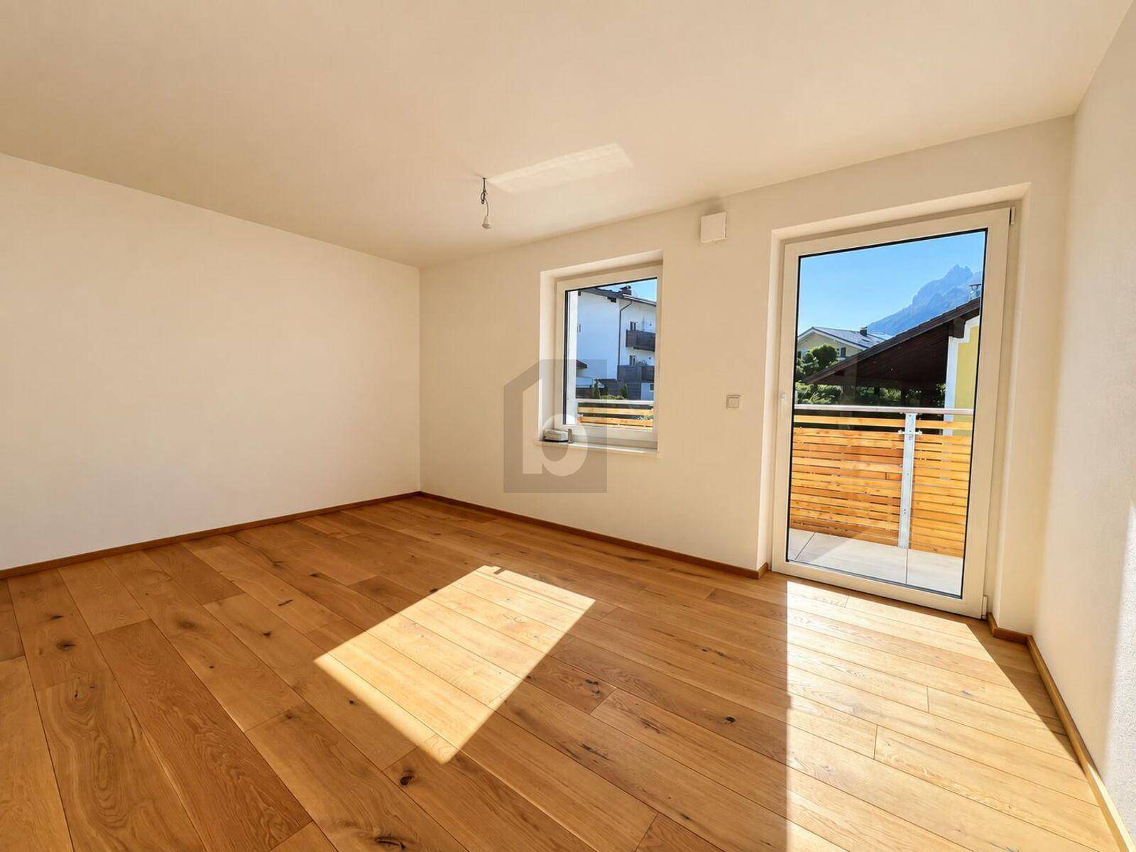 Heller, leerer Raum mit Holzboden und Zugang zu einem Balkon oder einer Terrasse.
