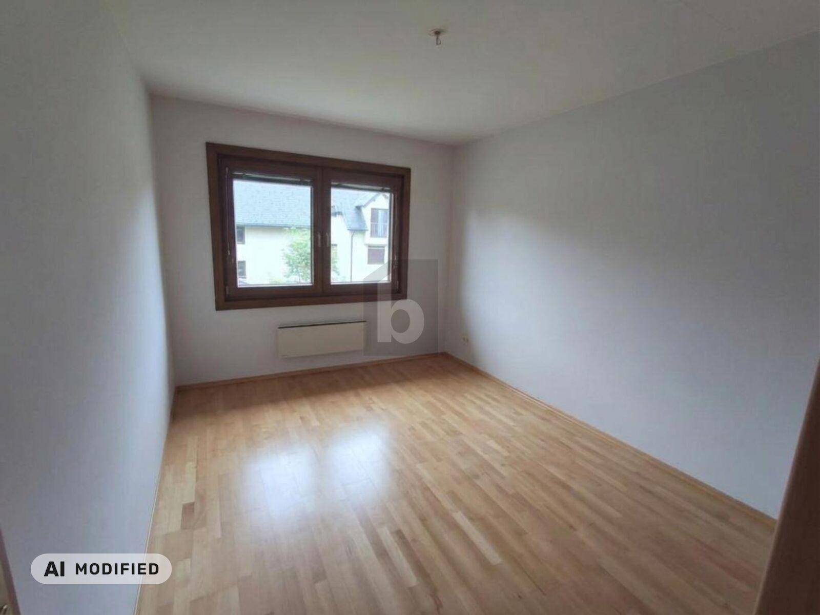 Leeres Schlafzimmer mit hellem Laminatboden und einem großen Fenster für Tageslicht.