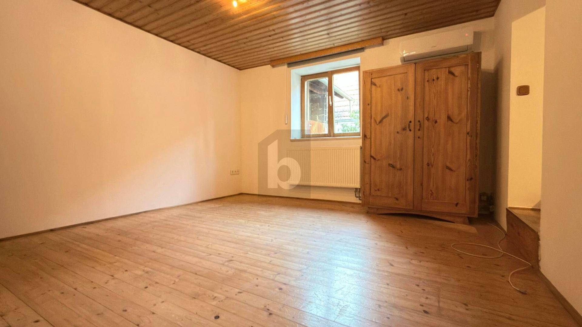 Helles Zimmer mit Holzboden, Holzdecke, Fenster und einem großen Holzschrank, ausgestattet mit Klimaanlage.
