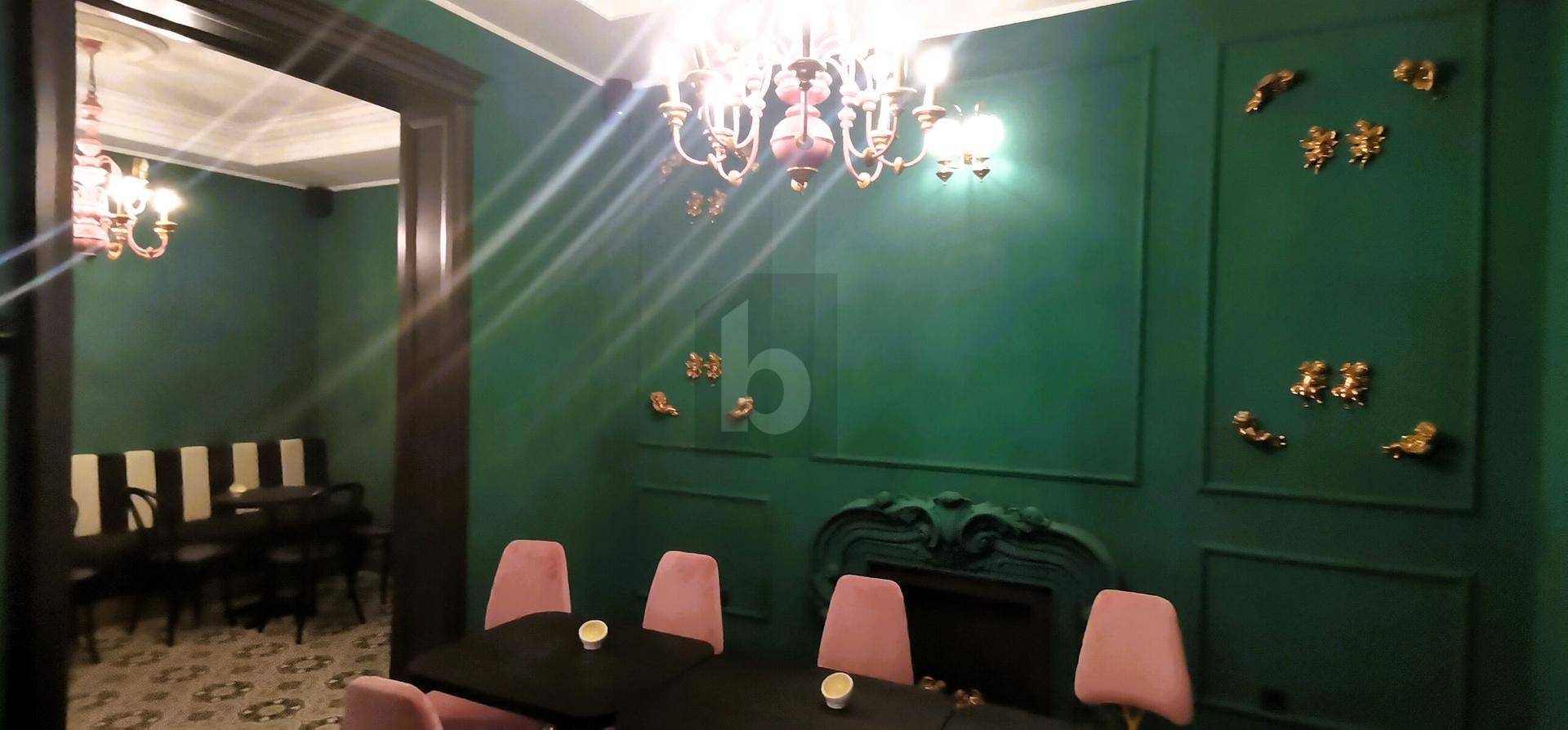Grüner Speisesaal mit rosa Stühlen, einem verzierten Kamin und einem klassischen Kronleuchter.
