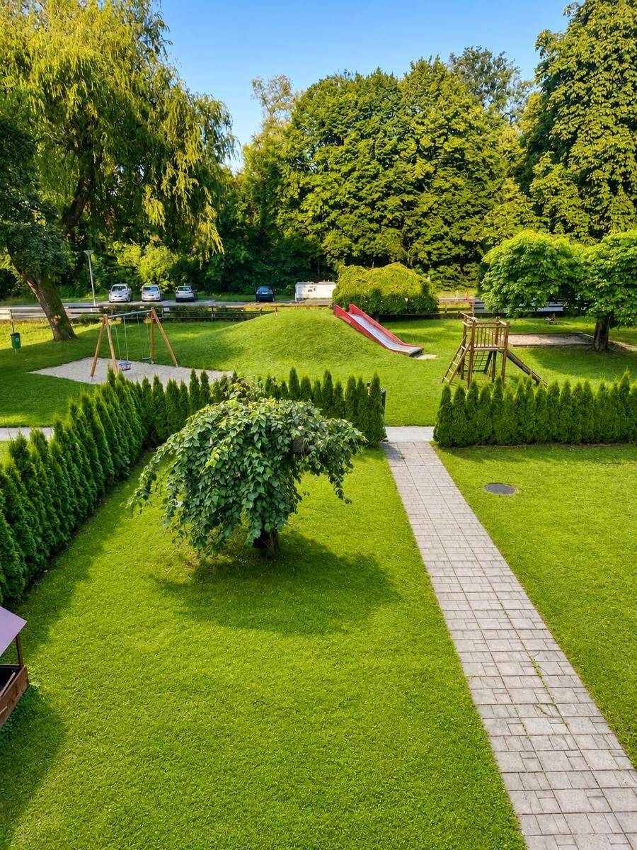 Gepflegter Gemeinschaftsgarten mit Rasenflächen, Hecken und Kinderspielplatz.