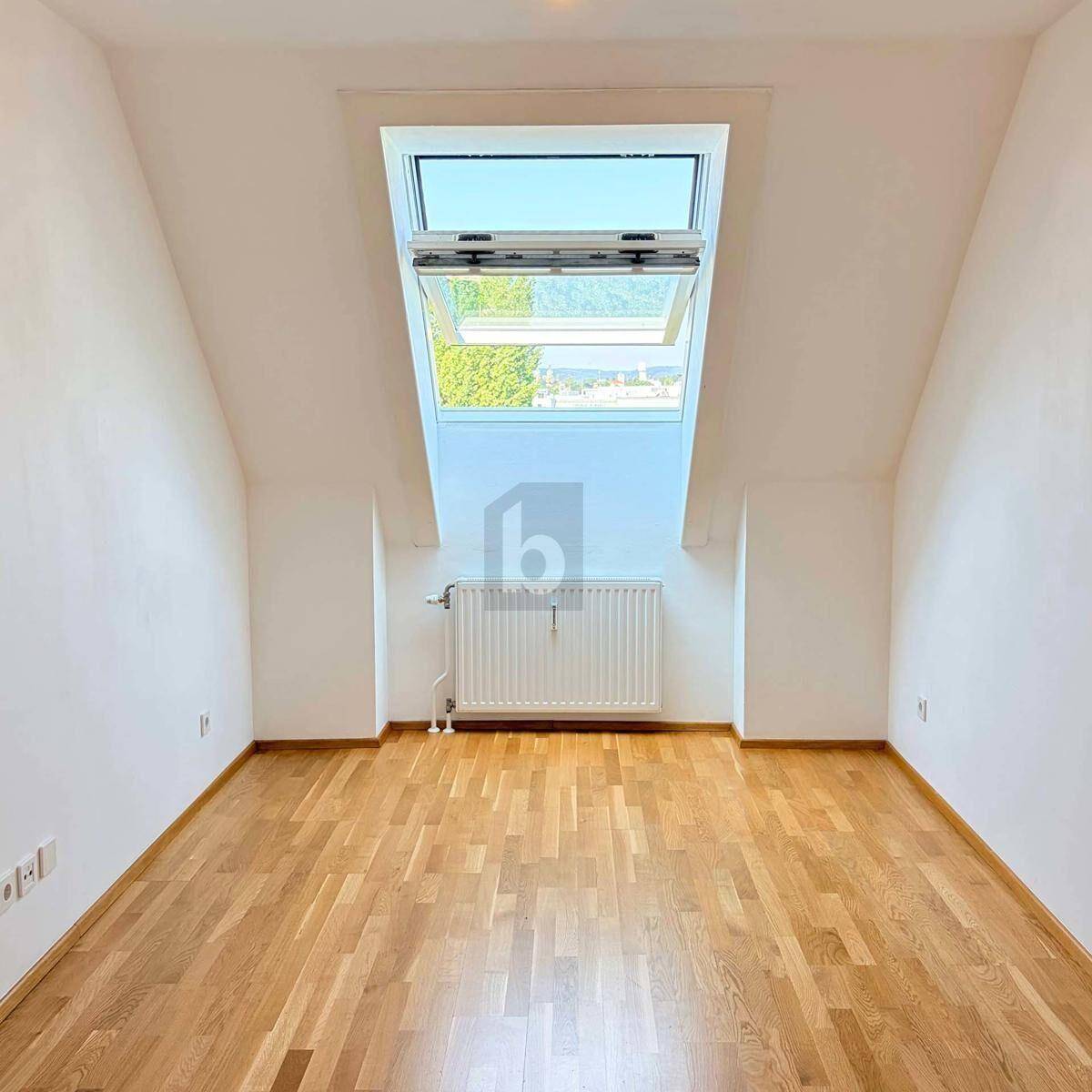 Helles Zimmer im Dachgeschoss mit Holzparkettboden, Dachschräge und großem Dachfenster.