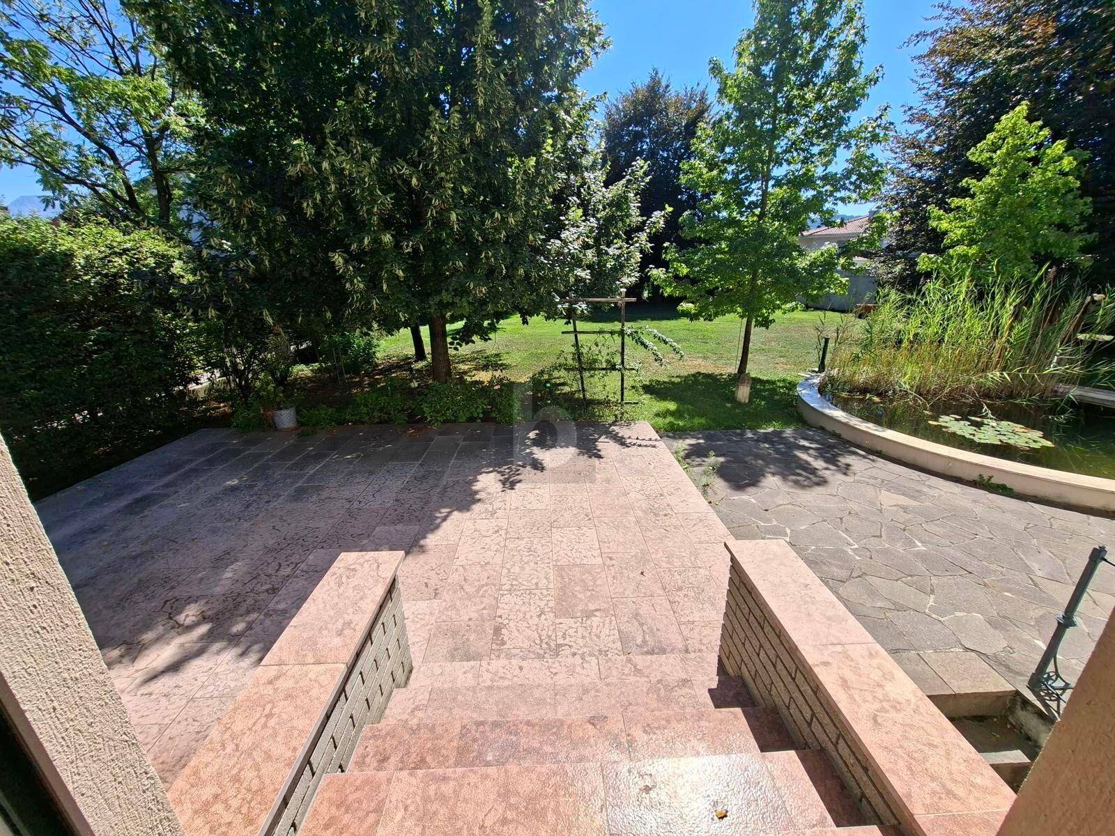 Große gepflasterte Terrasse mit Treppe, die zum Garten und einem Teich führt.