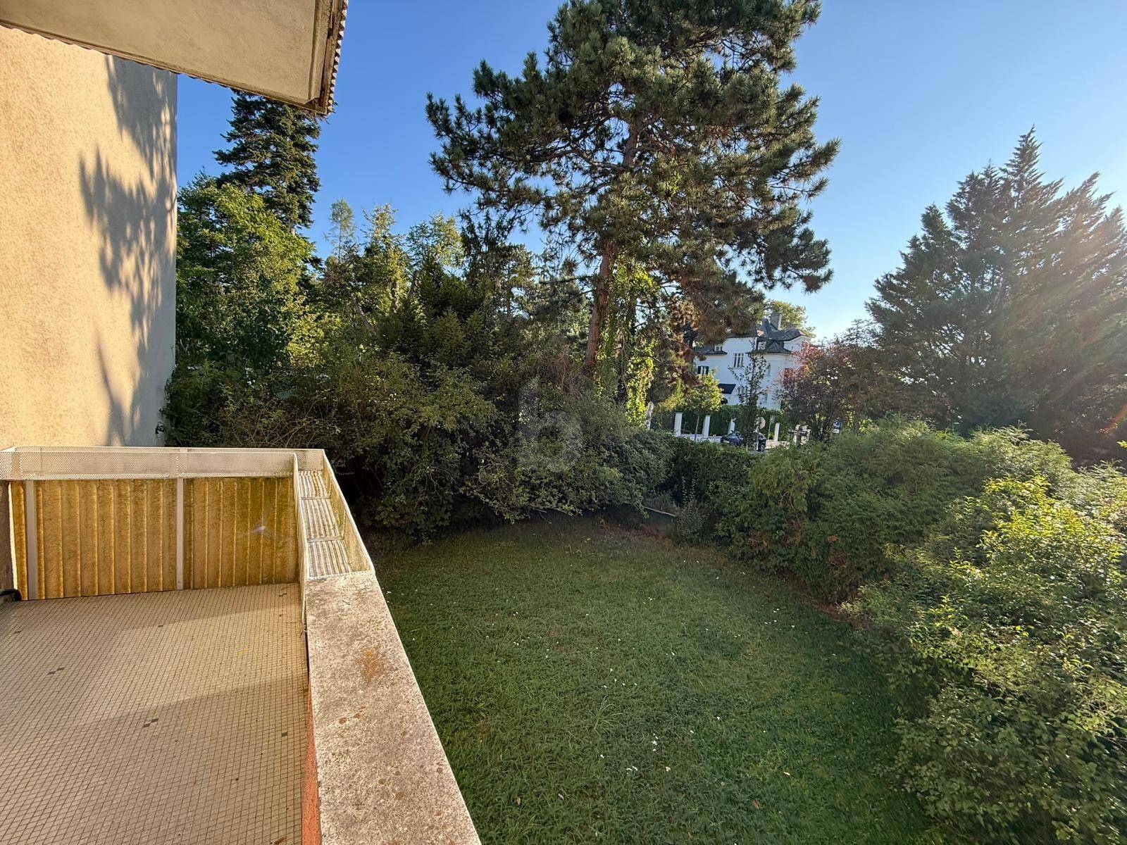 Balkon mit Blick auf einen gepflegten grünen Garten und hohe Bäume, ideal zum Entspannen im Freien.